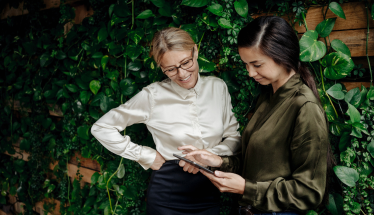 Two businesswomen in green office looking at tablet